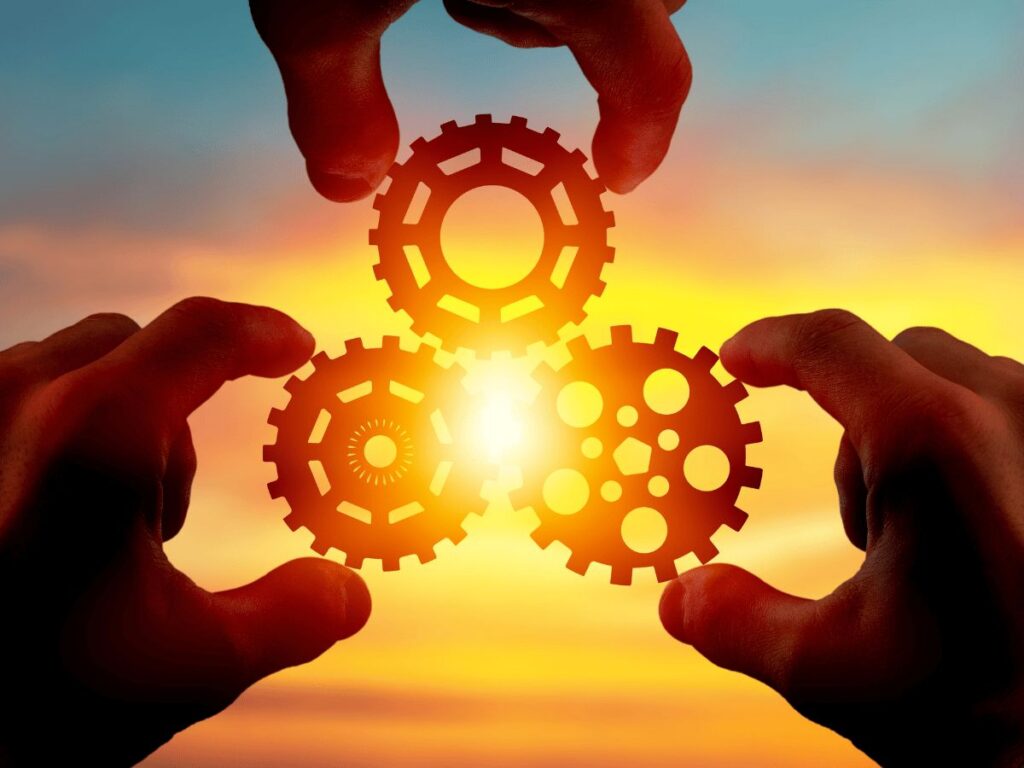 Three hands holding gear cogs with sun in the background